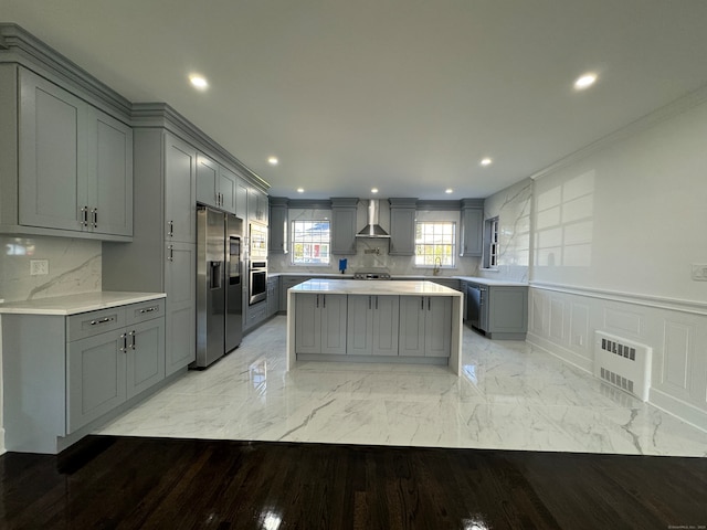 kitchen with a center island, wall chimney exhaust hood, tasteful backsplash, gray cabinets, and appliances with stainless steel finishes