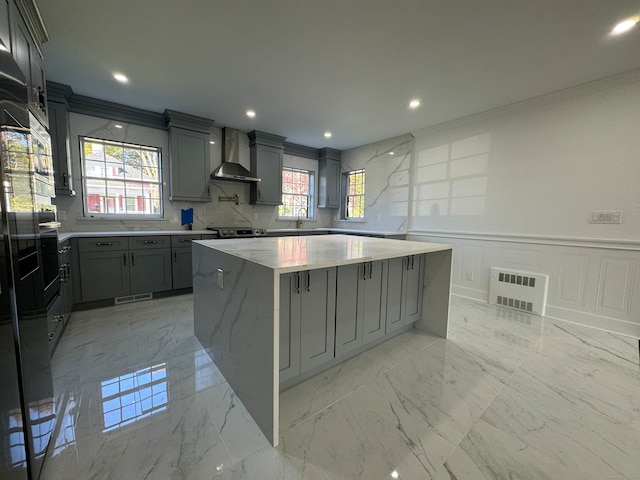 kitchen featuring light stone countertops, gray cabinetry, a large island, and wall chimney range hood