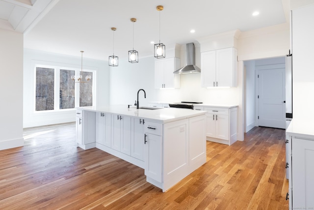 kitchen featuring a kitchen island with sink, sink, wall chimney exhaust hood, decorative light fixtures, and white cabinetry