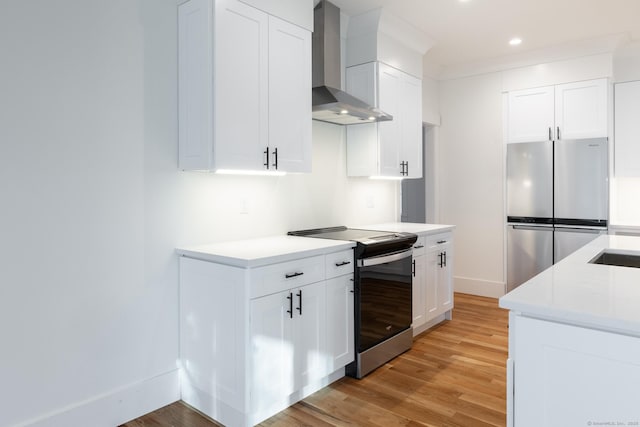 kitchen featuring wall chimney exhaust hood, crown molding, light hardwood / wood-style floors, white cabinets, and appliances with stainless steel finishes