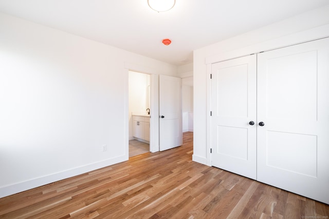 unfurnished bedroom featuring light wood-type flooring, connected bathroom, and a closet