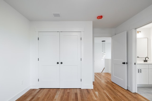 unfurnished bedroom with ensuite bathroom, light hardwood / wood-style flooring, a closet, and sink