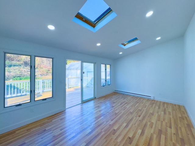 unfurnished room with vaulted ceiling with skylight, plenty of natural light, light hardwood / wood-style flooring, and a baseboard heating unit