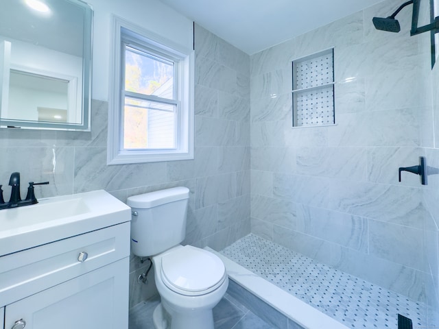 bathroom with tiled shower, vanity, toilet, and tile walls