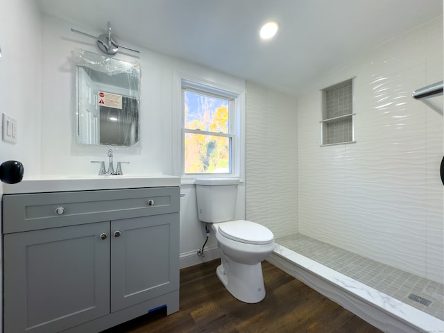 bathroom featuring vanity, lofted ceiling, hardwood / wood-style flooring, toilet, and tiled shower