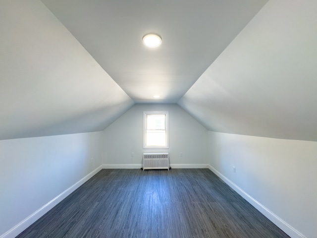 additional living space with radiator heating unit, dark wood-type flooring, and vaulted ceiling