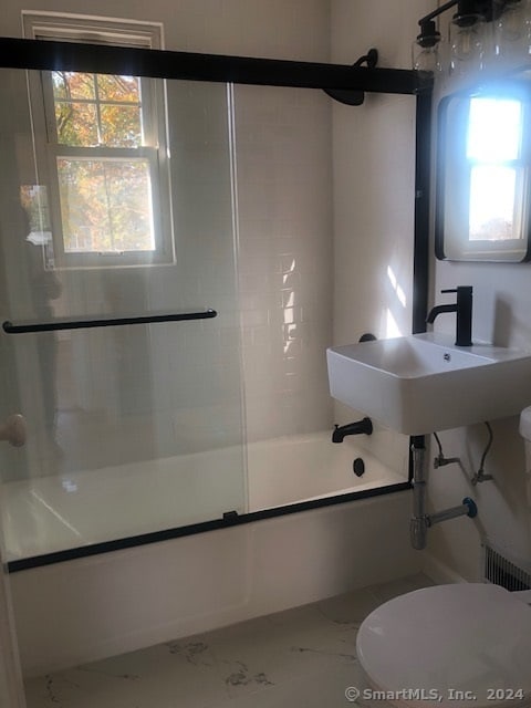 full bathroom with sink, toilet, a healthy amount of sunlight, and bath / shower combo with glass door