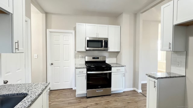 kitchen featuring decorative backsplash, light wood-type flooring, light stone counters, white cabinetry, and stainless steel appliances