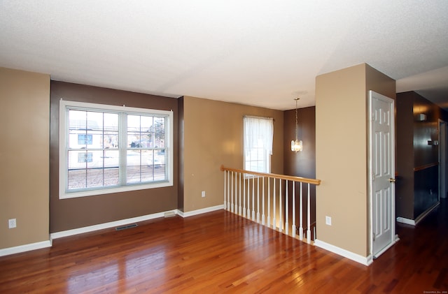 empty room with dark hardwood / wood-style flooring, a textured ceiling, a wealth of natural light, and an inviting chandelier