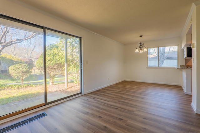 unfurnished dining area featuring visible vents, a notable chandelier, wood finished floors, and ornamental molding