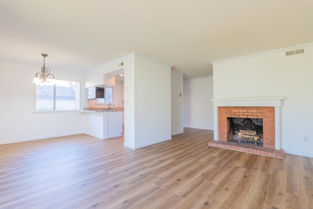 unfurnished living room with baseboards, visible vents, light wood-style flooring, ornamental molding, and a chandelier