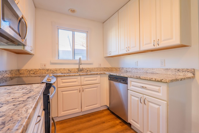 kitchen with light stone countertops, a sink, stainless steel appliances, white cabinets, and light wood-style floors