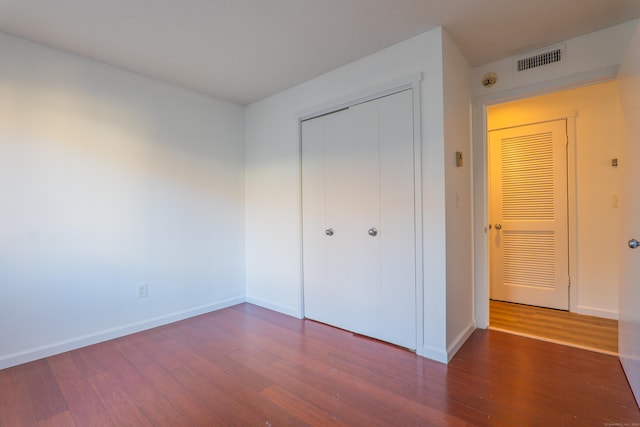 unfurnished bedroom featuring visible vents, baseboards, a closet, and wood finished floors