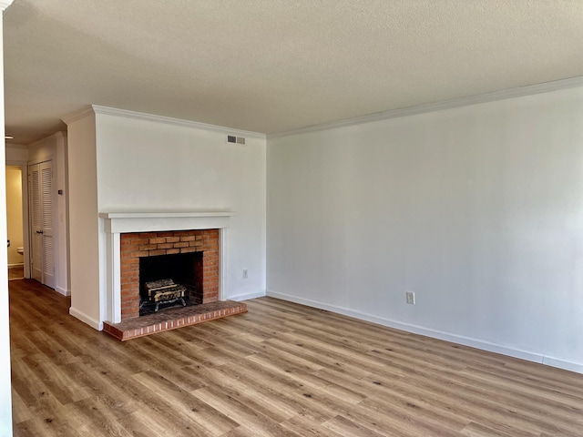 unfurnished living room with wood finished floors, baseboards, visible vents, ornamental molding, and a textured ceiling