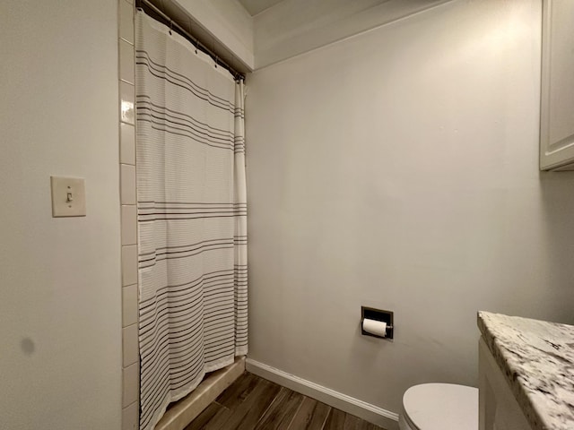 bathroom featuring curtained shower, baseboards, toilet, and wood finished floors