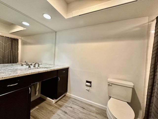 full bath with toilet, wood finished floors, recessed lighting, baseboards, and vanity