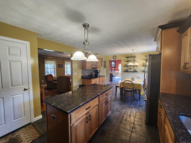 kitchen featuring stainless steel refrigerator, hanging light fixtures, a center island, decorative backsplash, and dark stone counters