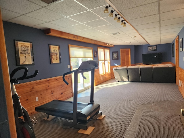 exercise room with rail lighting, carpet floors, a paneled ceiling, and wood walls