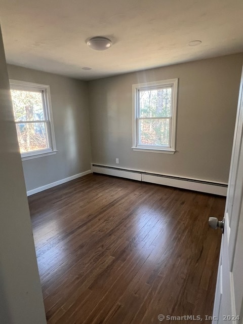 empty room featuring dark hardwood / wood-style floors, a wealth of natural light, and a baseboard heating unit