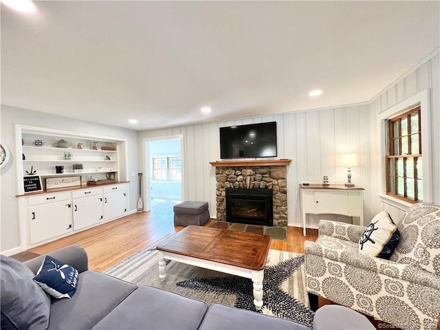 living room with built in shelves, a fireplace, and light wood-type flooring