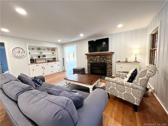 living room with wood-type flooring, a stone fireplace, and built in shelves