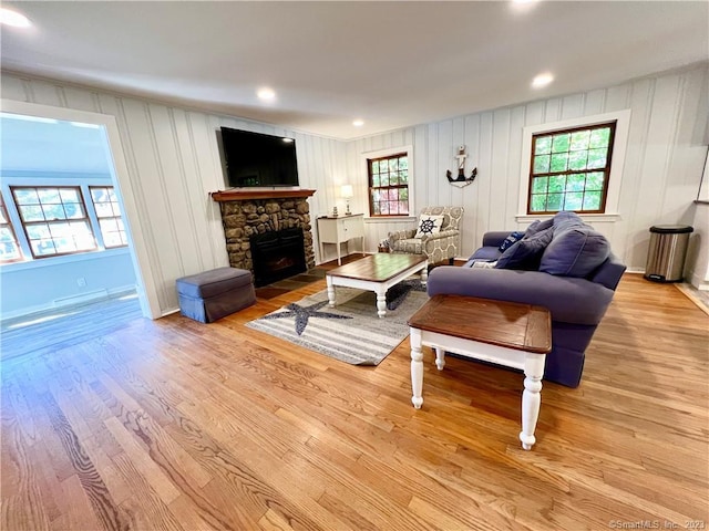 living room with light hardwood / wood-style flooring, a healthy amount of sunlight, and a stone fireplace