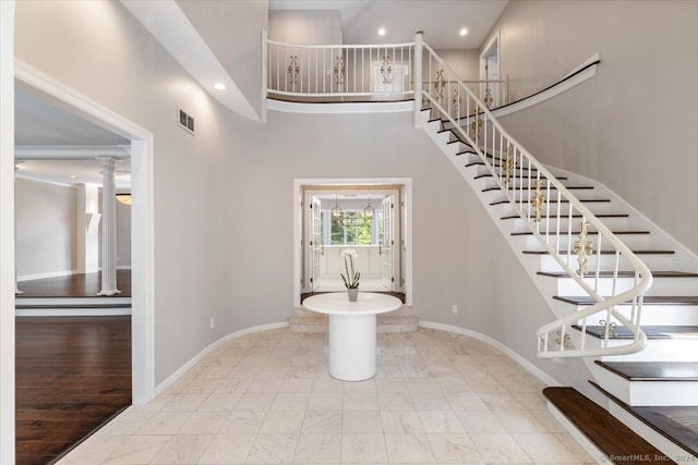 staircase with decorative columns, wood-type flooring, and a high ceiling