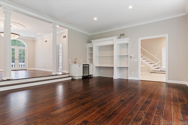 unfurnished living room with sink, crown molding, wine cooler, dark hardwood / wood-style flooring, and decorative columns