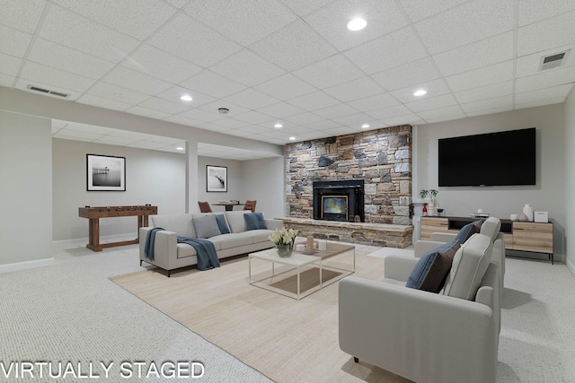 living room with a drop ceiling, a stone fireplace, and light carpet