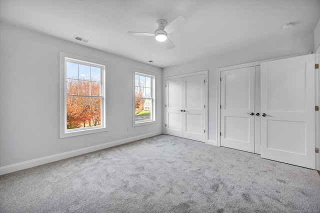 unfurnished bedroom featuring ceiling fan, light carpet, and multiple closets