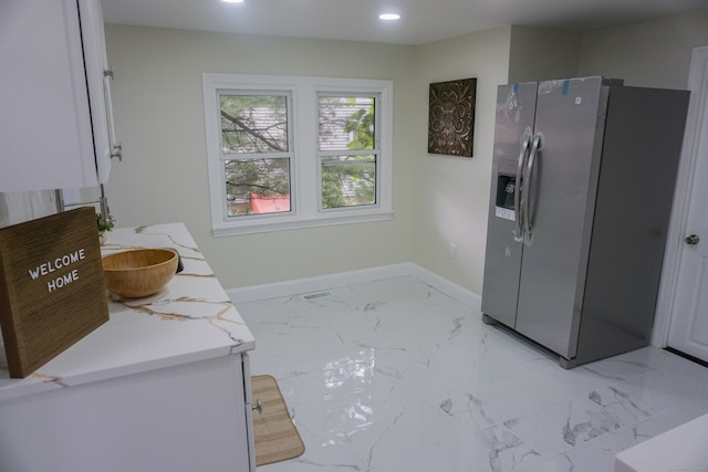 kitchen with light stone counters, white cabinetry, and stainless steel refrigerator with ice dispenser