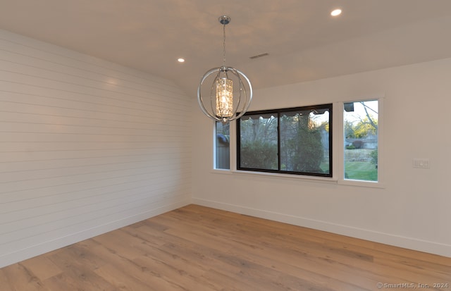 empty room with wood-type flooring, lofted ceiling, and an inviting chandelier