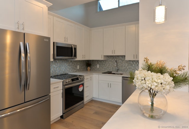 kitchen featuring white cabinetry, sink, light hardwood / wood-style floors, pendant lighting, and appliances with stainless steel finishes