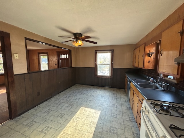 kitchen featuring dishwasher, wood walls, white gas stove, and sink