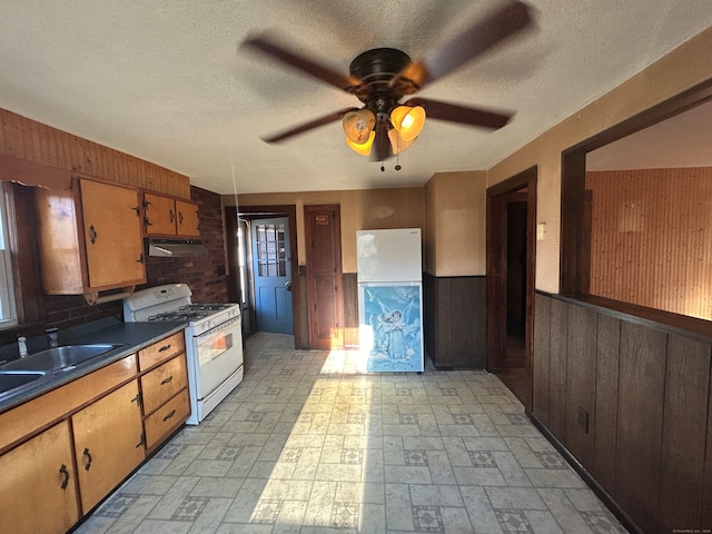 kitchen with a textured ceiling, wooden walls, ceiling fan, and white appliances