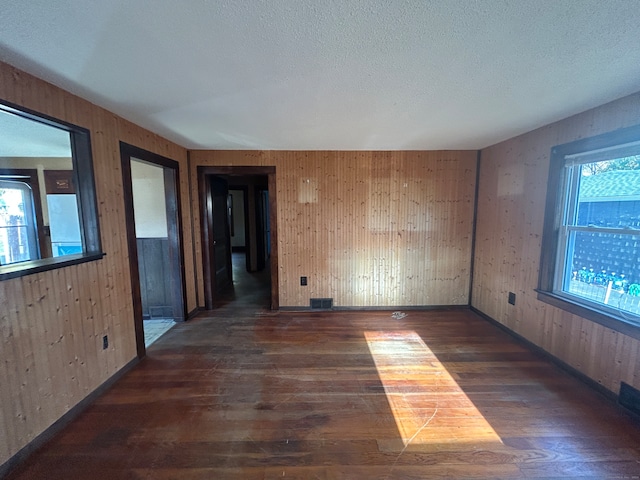 spare room with a textured ceiling, wood walls, and dark hardwood / wood-style floors