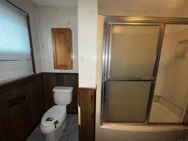 bathroom featuring toilet, a shower with door, and wood walls