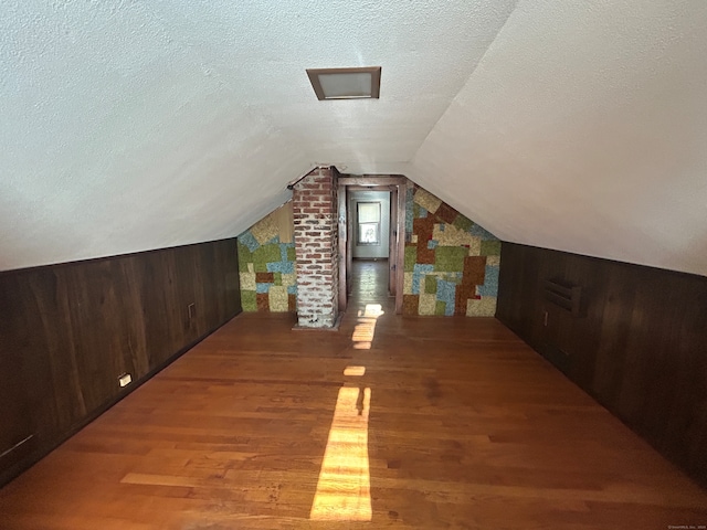 bonus room featuring a textured ceiling, hardwood / wood-style flooring, vaulted ceiling, and wood walls