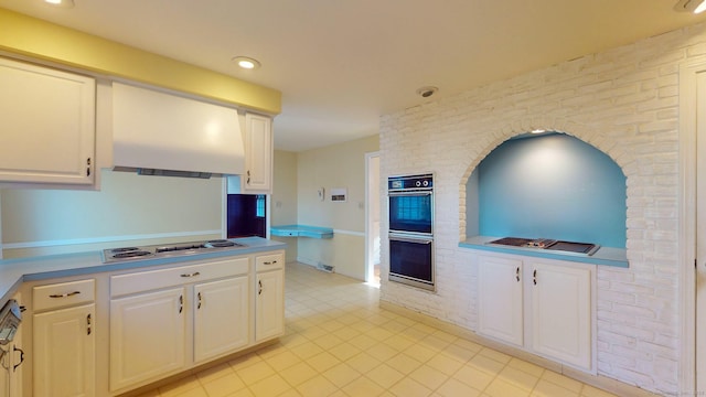 kitchen with white gas stovetop, white cabinetry, double oven, and range hood