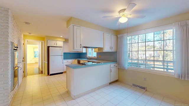 kitchen featuring kitchen peninsula, a wealth of natural light, ceiling fan, white refrigerator, and white cabinetry