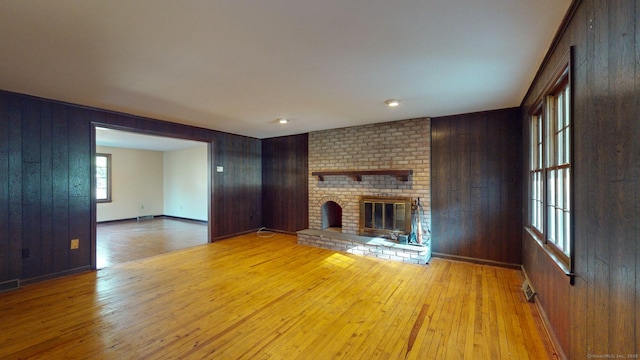 unfurnished living room with a fireplace, light hardwood / wood-style floors, and wooden walls