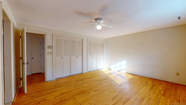 unfurnished bedroom featuring ceiling fan, light hardwood / wood-style floors, and multiple closets