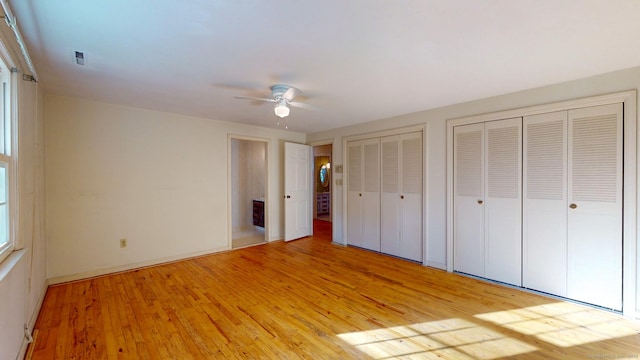 unfurnished bedroom featuring light hardwood / wood-style flooring, ceiling fan, and multiple closets