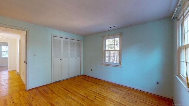 unfurnished bedroom with multiple windows, a closet, and light wood-type flooring