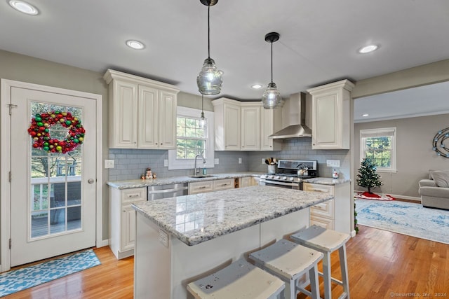 kitchen featuring backsplash, light hardwood / wood-style flooring, wall chimney exhaust hood, a kitchen island, and stainless steel appliances