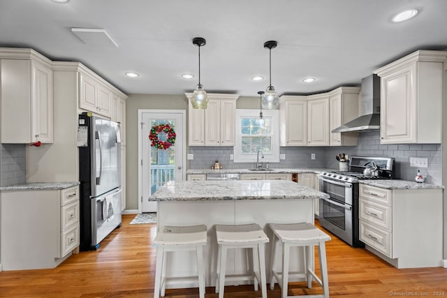 kitchen with a kitchen island, light hardwood / wood-style floors, wall chimney range hood, and appliances with stainless steel finishes