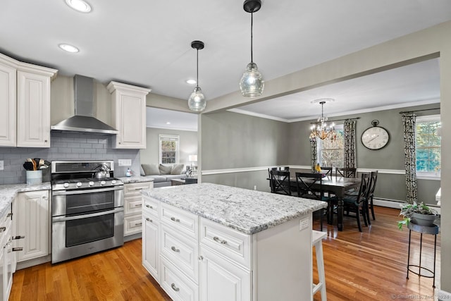 kitchen featuring light wood-type flooring, crown molding, wall chimney range hood, stainless steel range oven, and white cabinets