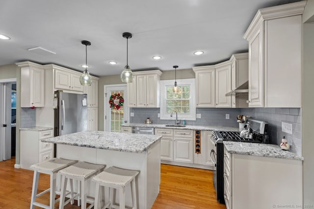 kitchen featuring stainless steel appliances, sink, decorative light fixtures, light hardwood / wood-style flooring, and a kitchen island