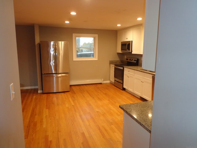 kitchen featuring appliances with stainless steel finishes, baseboard heating, dark stone countertops, light hardwood / wood-style floors, and white cabinetry