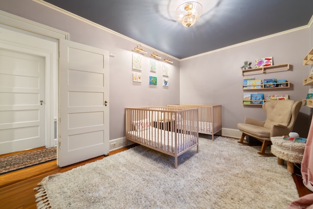 bedroom featuring crown molding, a nursery area, and wood-type flooring